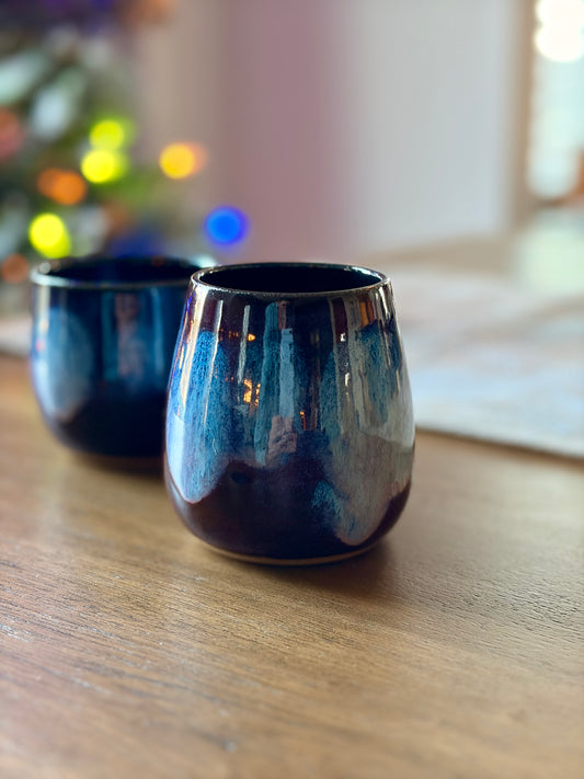 Two purple and blue ceramic cups on a wooden surface with a blurred colorful background