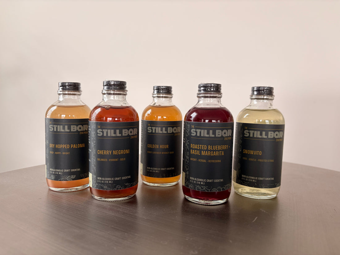 The Still Bar's five zero-proof cocktail bottles lined up on a bar, non-alcoholic craft cocktails for Sober October and Dry January