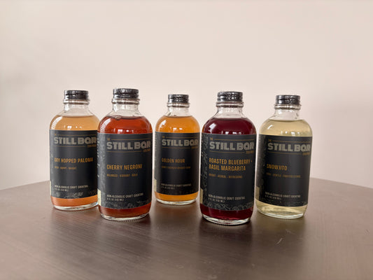 The Still Bar's five zero-proof cocktail bottles lined up on a bar, non-alcoholic craft cocktails for Sober October and Dry January