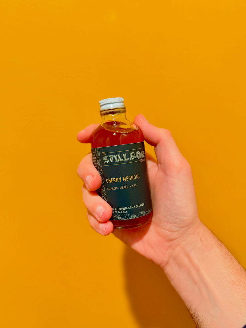 Hand holding a bottle of Cherry Negroni against a yellow background