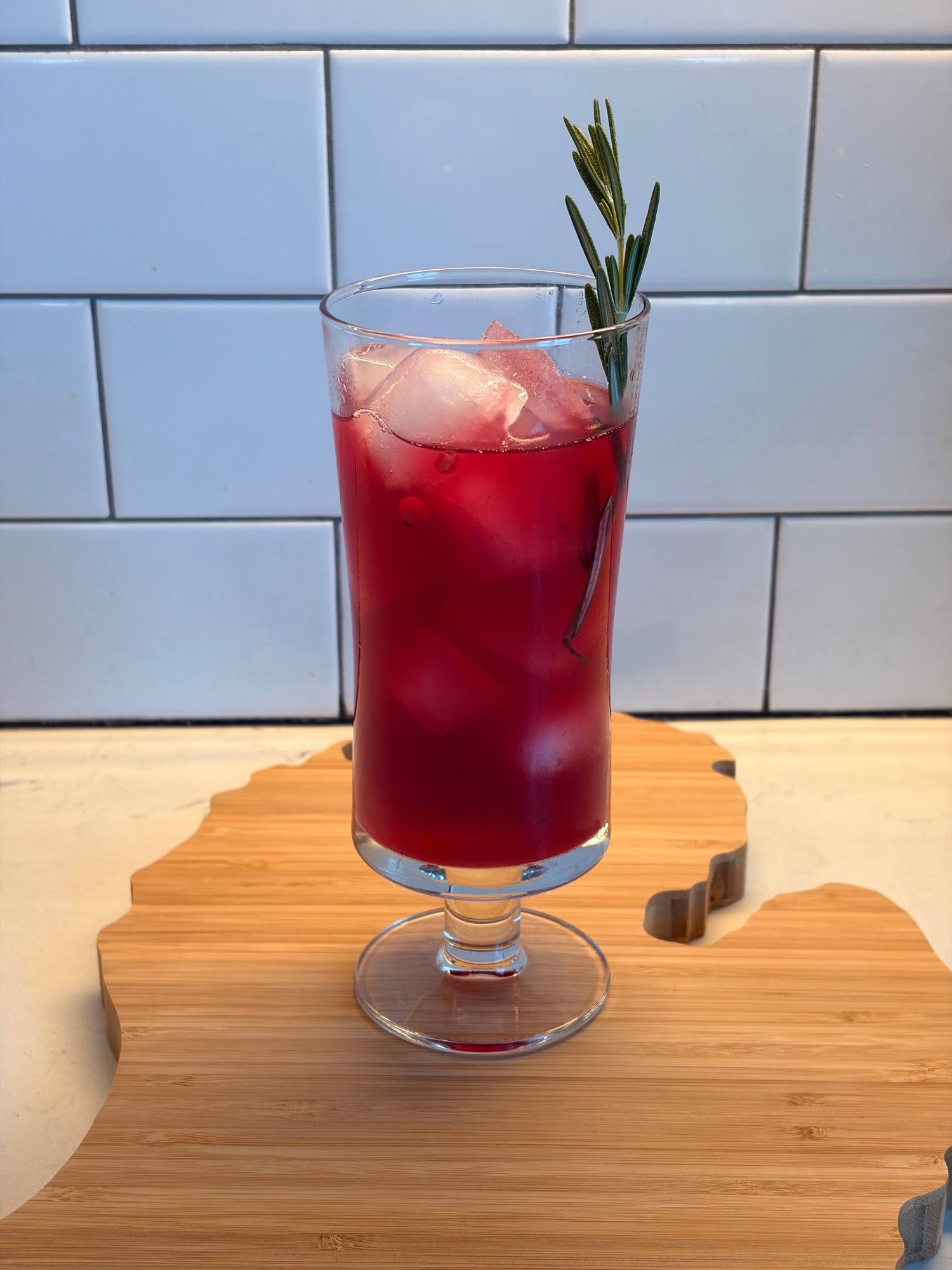 Red cocktail with a sprig of rosemary in a glass on a wooden surface.