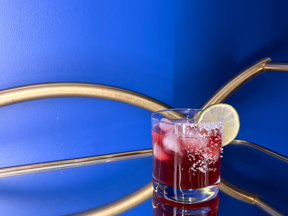 Non-alcoholic blueberry basil margarita over ice in a salt-rimmed glass with a lime wedge