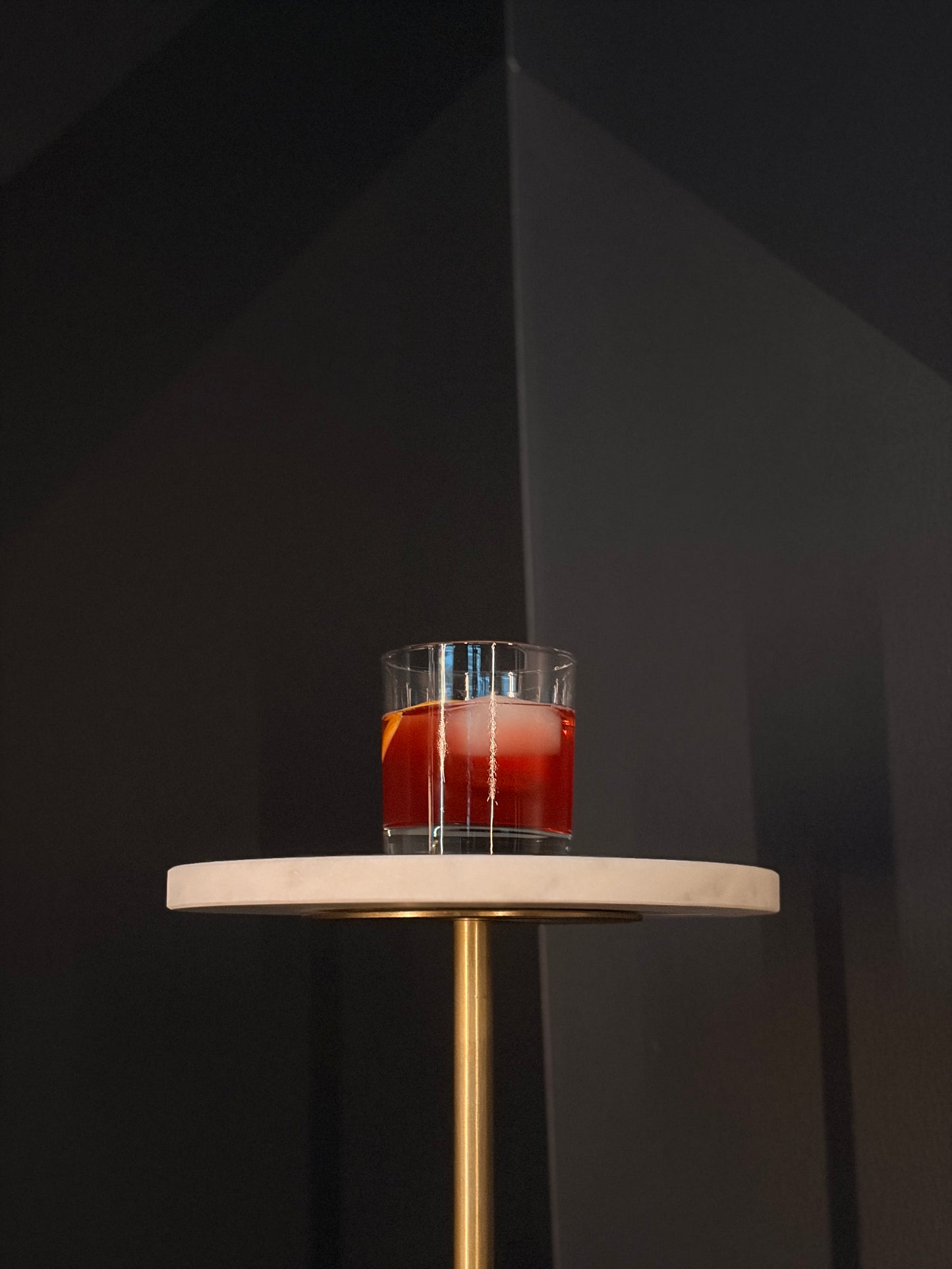 Cherry Negroni on a round table in front of a black wall