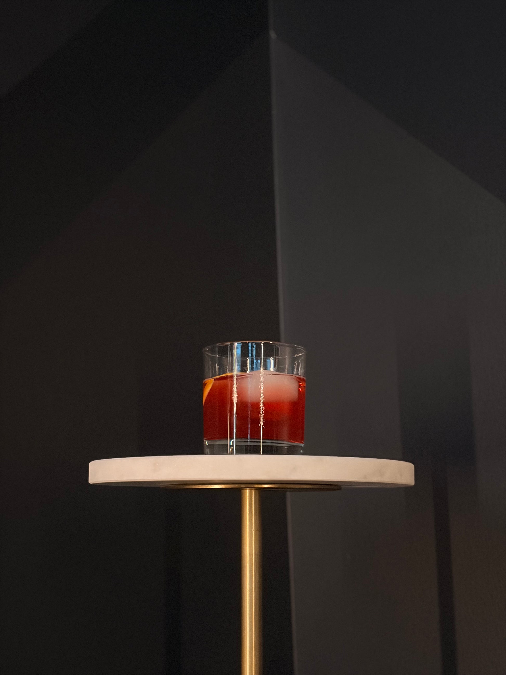 Cherry Negroni on a round table in front of a black wall