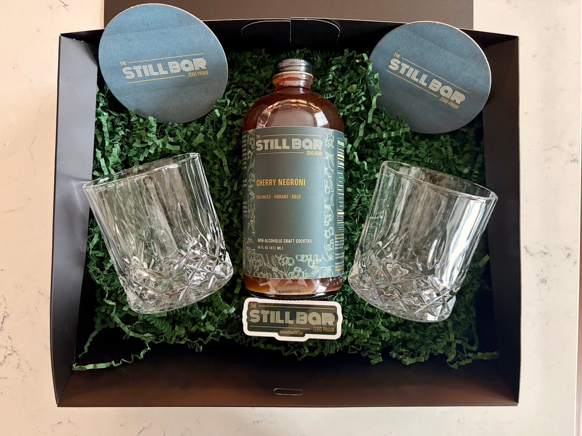 The Still Bar cherry negroni bottle with two glasses in a decorative box on a light background