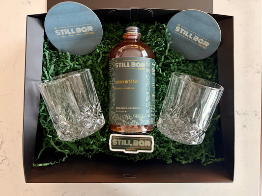The Still Bar cherry negroni bottle with two glasses in a decorative box on a light background