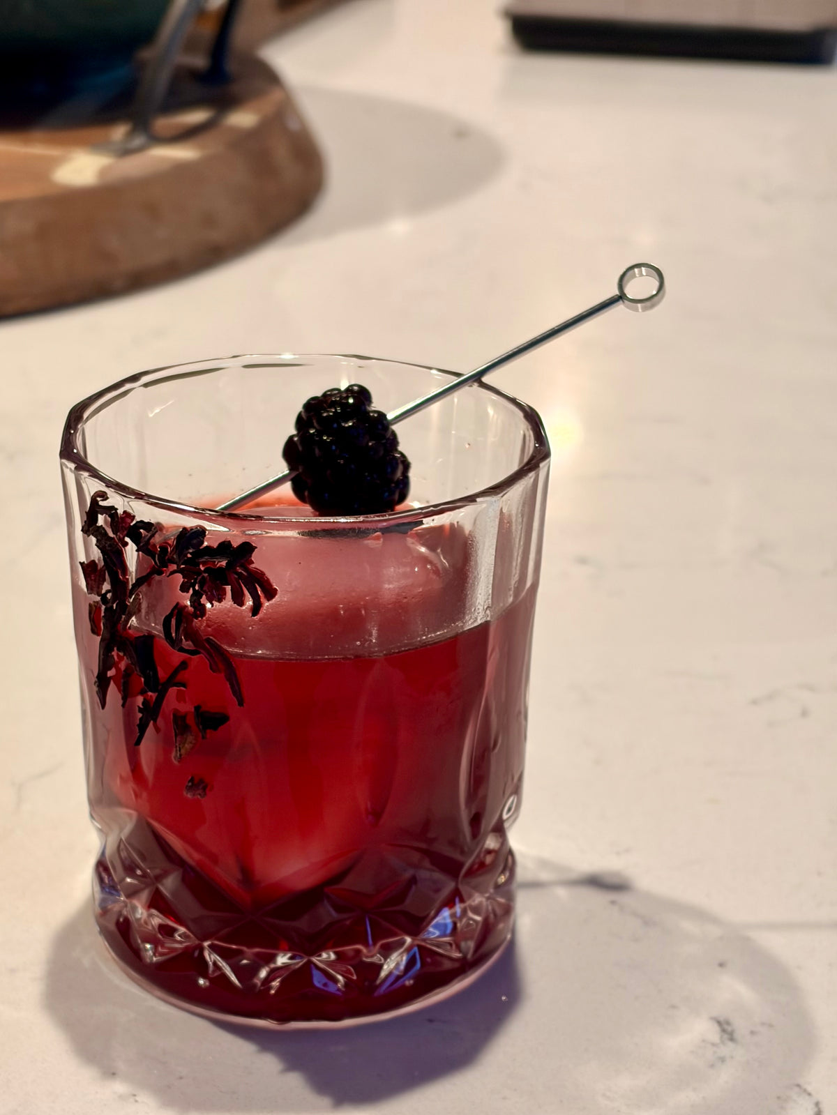 Red cocktail in a glass with a blackberry garnish on a white surface